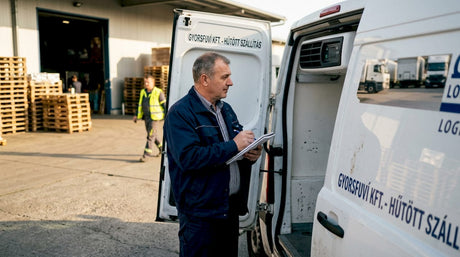 A logisztikai vezető a parkolóban áll a hűtős furgon mellett